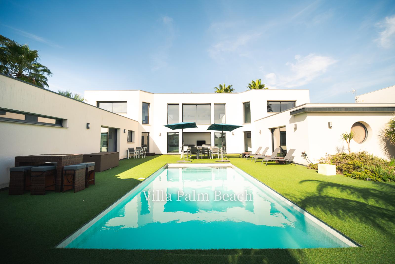 La piscine chauffée face à la villa blanche, parasols et palmiers sous un ciel bleu